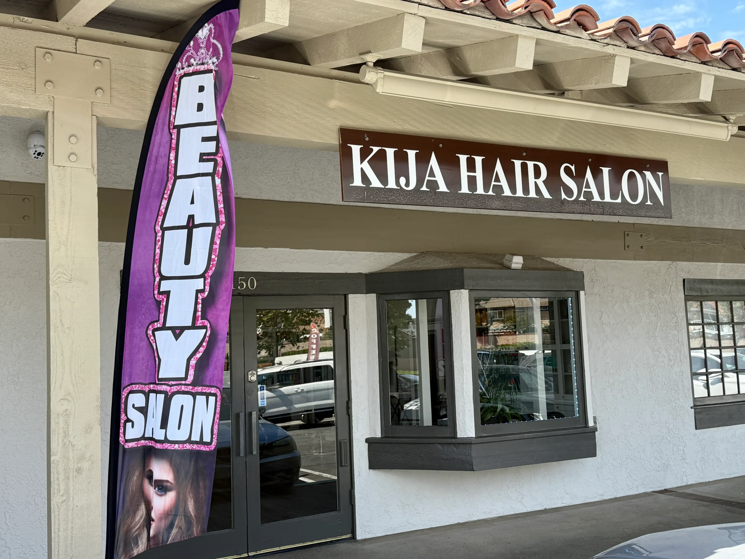 Exterior front view of Kija Hair Salon in Irvine, showing the salon entrance, signage, and a purple “Beauty Salon” feather flag next to the door.